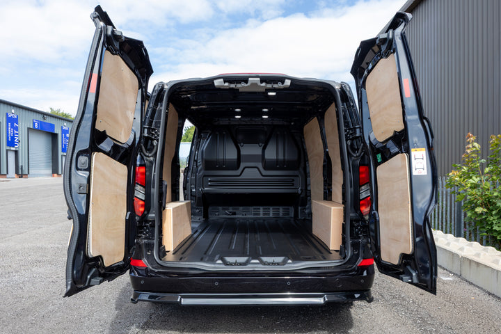Rear view of a black cargo van with both side doors open, showing the open cargo area and light tan interior panels in an outdoor lot.