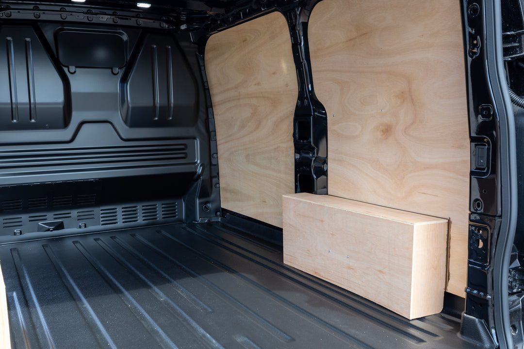 Custom plywood cargo side walls installed inside a black van, with a matching wooden storage box placed on the floor.