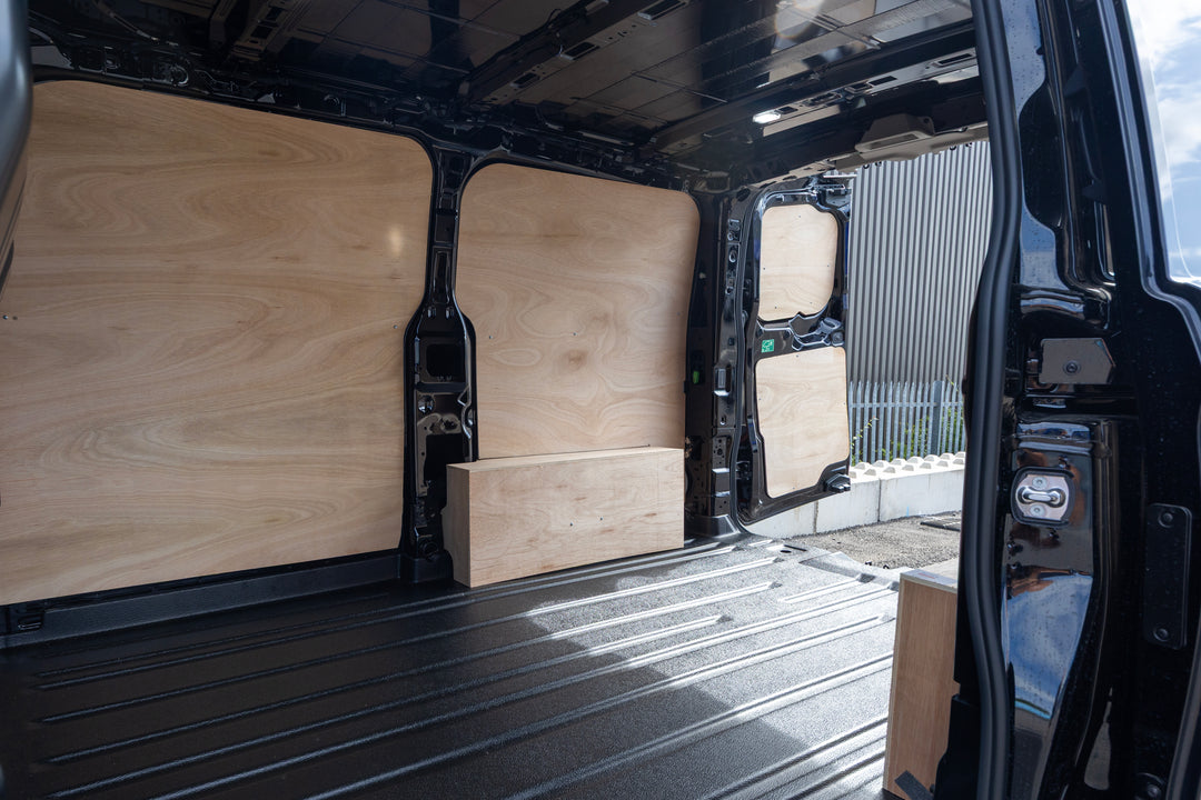 Custom plywood cargo partition panels installed inside a black van, showing the light wood grain surfaces and a matching wooden storage box on the floor.
