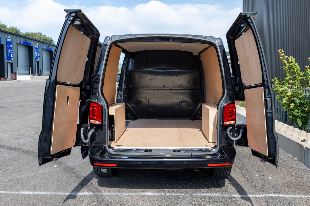 Rear view of a black van with both side cargo doors open, showing a custom light tan interior cargo area and side panels in an outdoor lot.