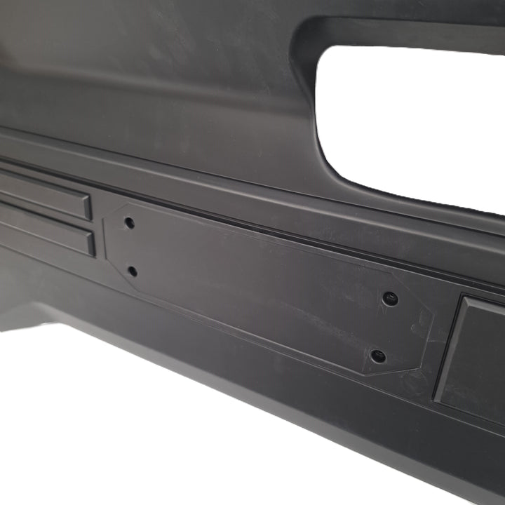 Close-up of a black moulded plastic tailgate cover from sterling automotive part with molded details, mounting holes for the missing O letter, and a recessed slot, shown against a white background.
