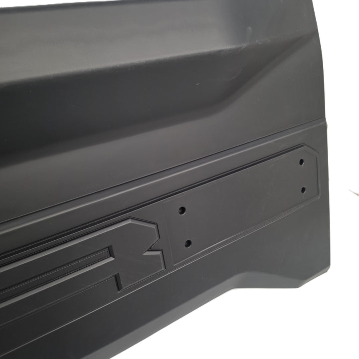 Close-up of a black moulded plastic tailgate cover from sterling automotive part with molded details, mounting holes for the missing D letter, and a recessed slot, shown against a white background.
