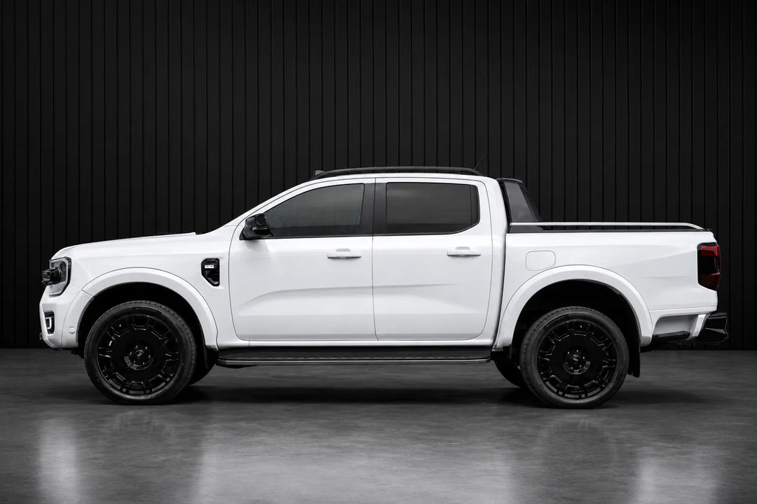 A white Ford Ranger pickup truck shown from a side profile view, fitted with black aftermarket wheels and black window tint, set against a dark gray studio background.