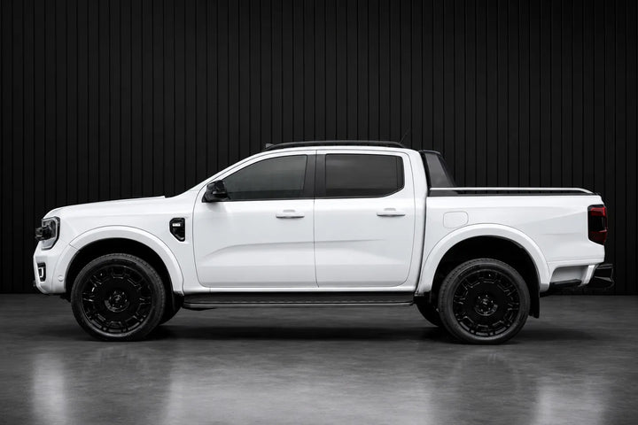 A white Ford Ranger pickup truck shown from a side profile view, fitted with black aftermarket wheels and black window tint, set against a dark gray studio background.
