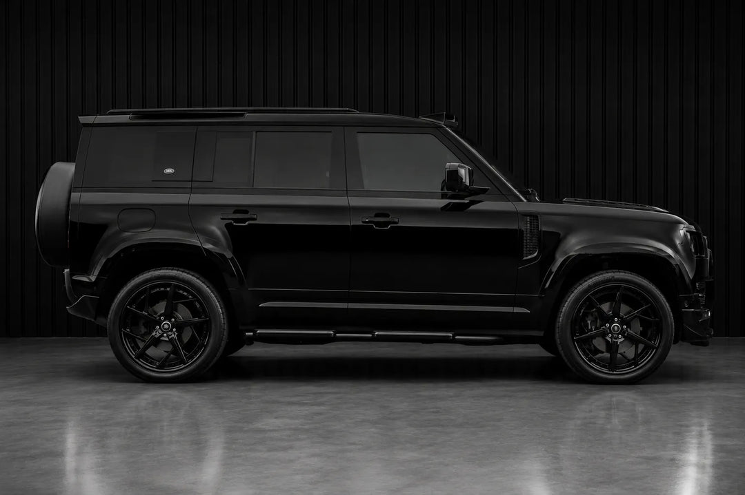 A black SUV shown in full side profile against a dark studio backdrop with a reflective floor.