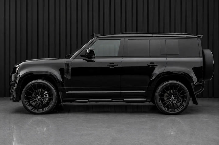 A black SUV shown in a side profile view against a dark gray corrugated metal wall and concrete floor.