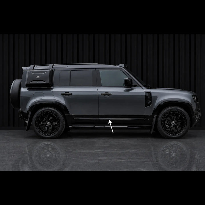 A dark gray SUV shown in a side profile view against a black slatted wall, with a white arrow pointing to the Lower Door Cladding step bars.