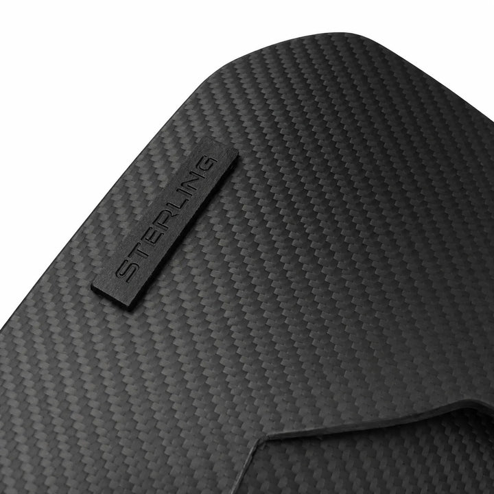 A close-up of a black carbon fiber textured mat with a small metal brand tab embossed with the word 'STERLING'.