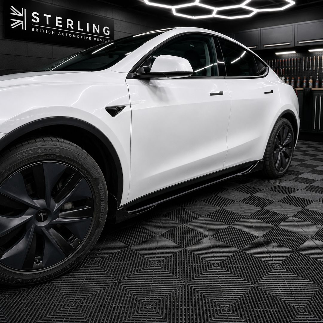 A white Tesla Model Y is parked inside a black garage or showroom with a black-and-gray checkered floor and a Sterling brand sign on the wall.