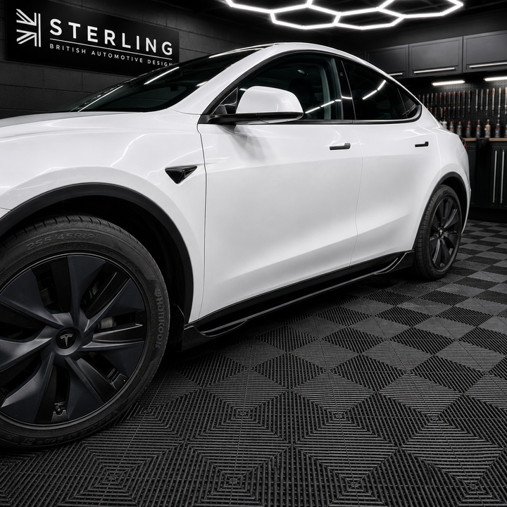 A white Tesla Model Y is parked inside a black garage or showroom with a black-and-gray checkered floor and a Sterling brand sign on the wall.