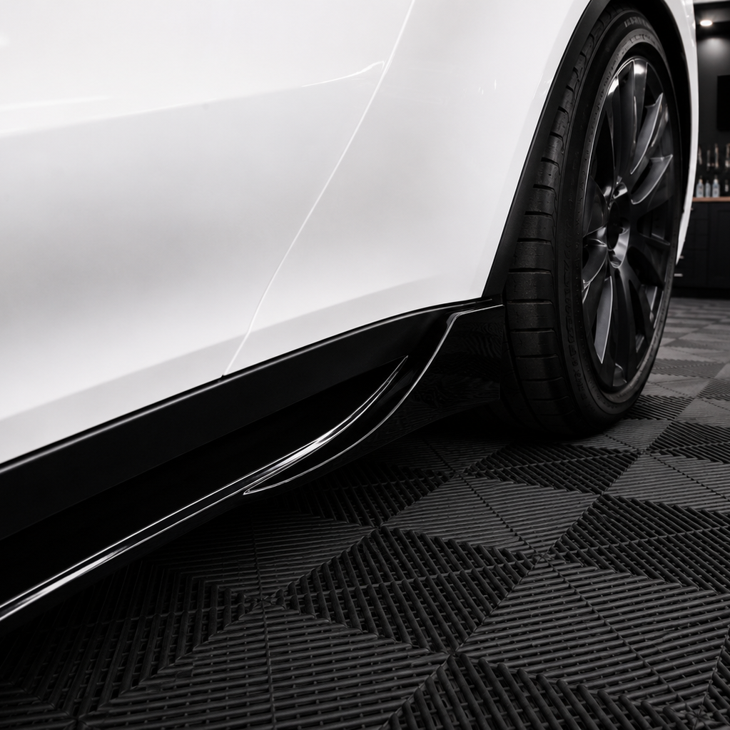 A close-up of a white car's side bodywork and black wheel, positioned over a black and gray checkered floor inside a garage. A Sterling branded sign is visible on the wall in the background.