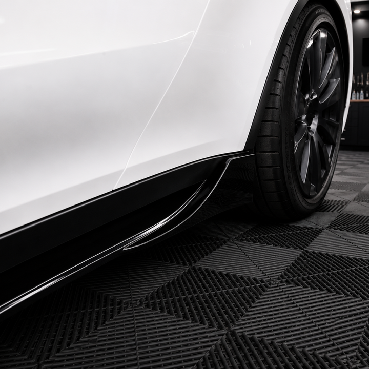 A close-up of a white car's side bodywork and black wheel, positioned over a black and gray checkered floor inside a garage. A Sterling branded sign is visible on the wall in the background.