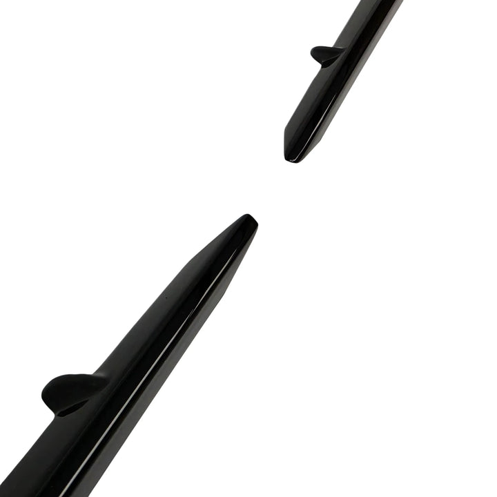 An close angled shot of a pair of glossy black plastic dual notch fog light surround body trim pieces, shown as a pair, on a plain white background.