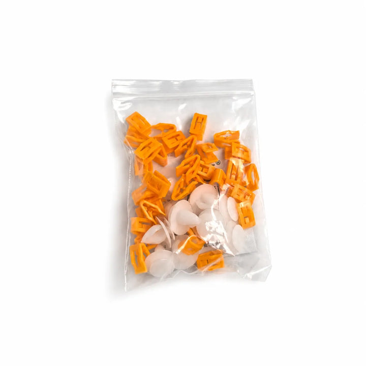 A clear plastic zip-top bag containing small orange plastic clips and several white plastic pieces, photographed on a plain white background.


