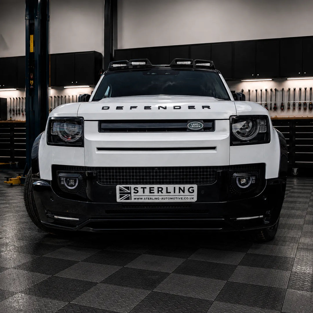 A white Land Rover Defender with a black front bumper lip and a custom license plate reading 'STERLING' is photographed in the sterling garage setting.