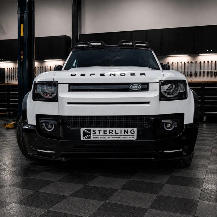 A white Land Rover Defender with a black front bumper lip and a custom license plate reading 'STERLING' is photographed in the sterling garage setting.