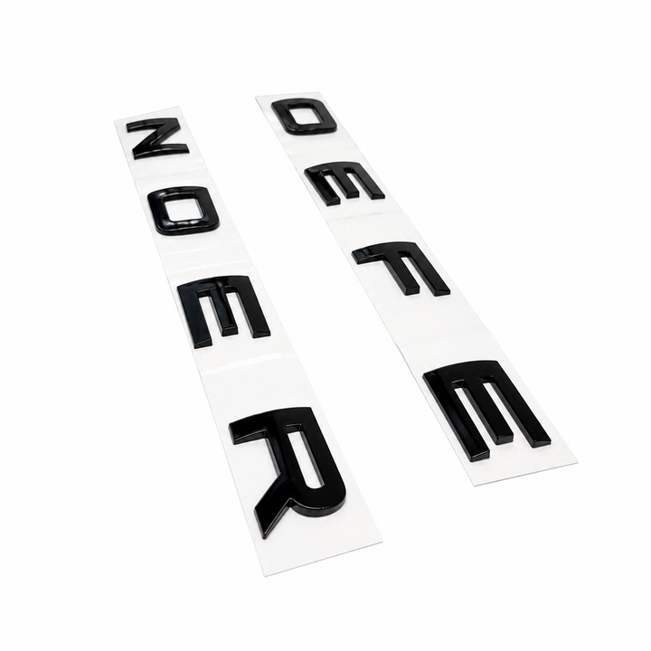 Two strips of glossy black raised letter decals on white backing sheets, arranged diagonally on a plain white background.