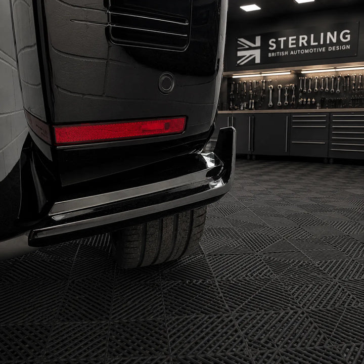 A close-up of a black Defender rear lower bumper and canards, with a visible Sterling automotive design sign in the background inside a workshop or garage.