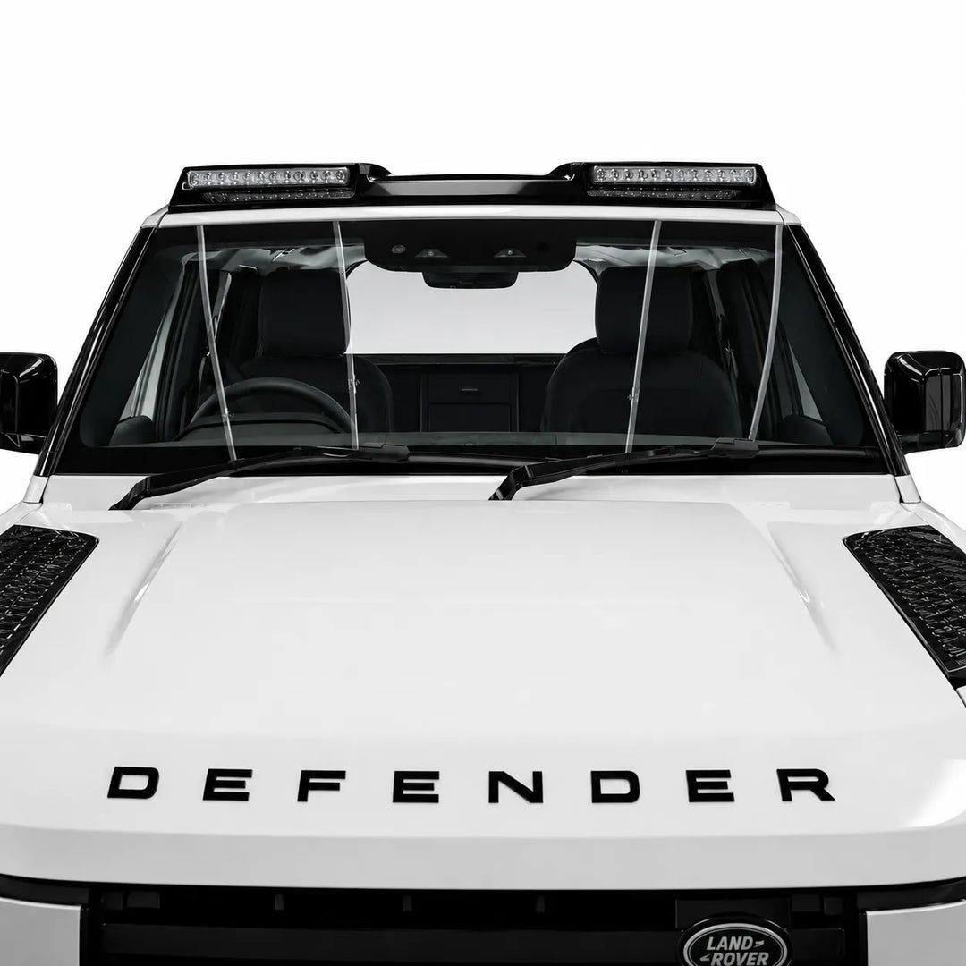 A pair of clear windshield wiper guards installed on the front windshield of a white Land Rover Defender, shown against a solid white background.