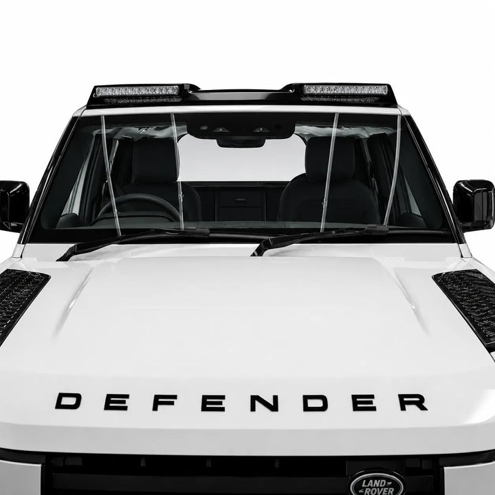 A pair of clear windshield wiper guards installed on the front windshield of a white Land Rover Defender, shown against a solid white background.