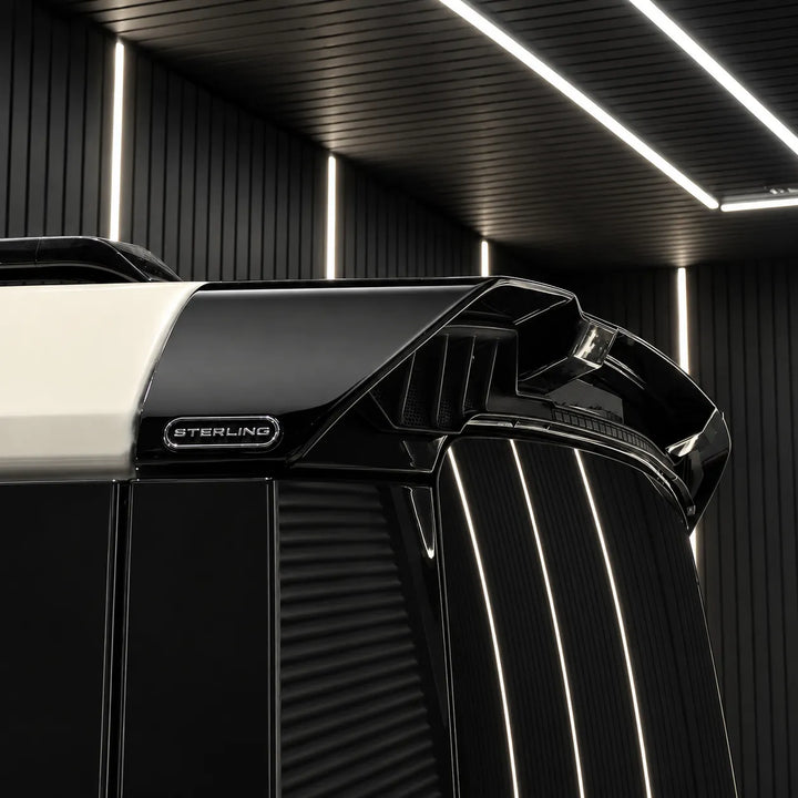 Close-up of a black Sterling Defender vehicle body panel with a visible Sterling badge, set against a dark modern interior with illuminated ceiling lines.