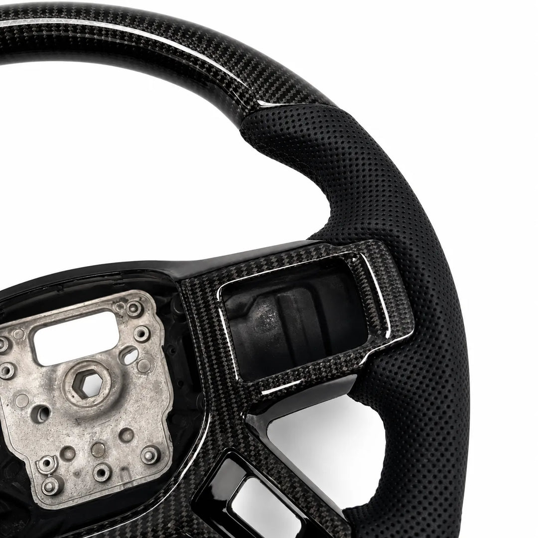 Close-up of a carbon fiber steering wheel with a black perforated leather or vinyl wrap on the outer rim, showing the wheel's inner structure and mounting area against a white background.