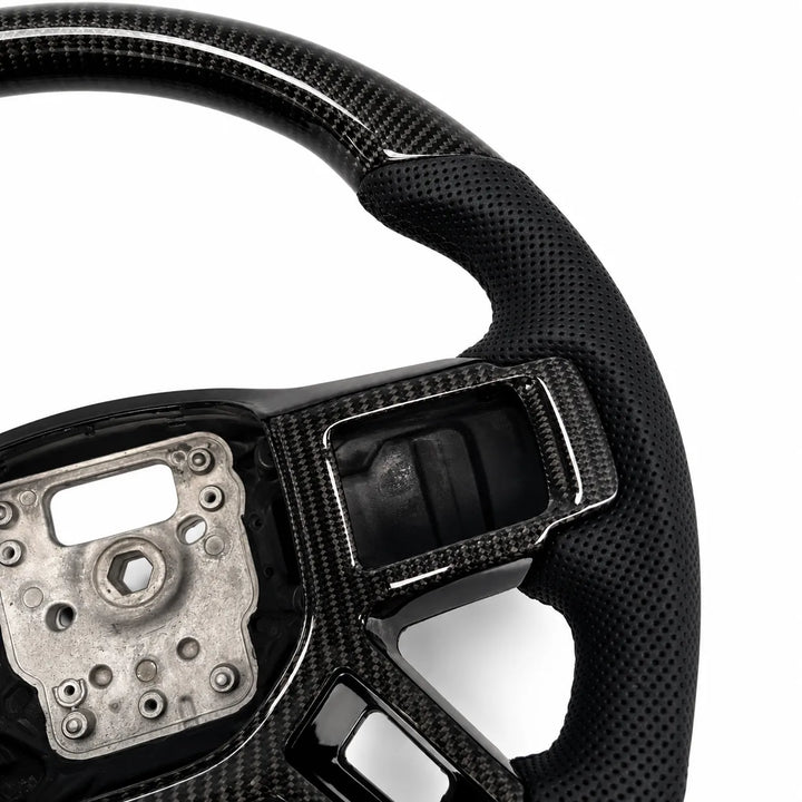 Close-up of a carbon fiber steering wheel with a black perforated leather or vinyl wrap on the outer rim, showing the wheel's inner structure and mounting area against a white background.