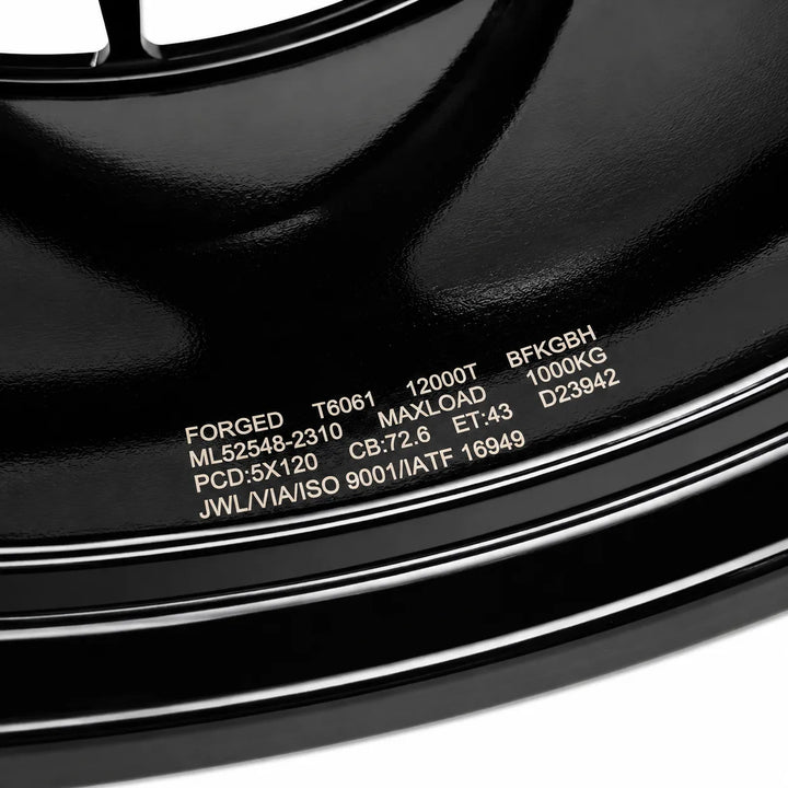 Close-up of a black forged steel wheel rim with white printed specifications on the side.