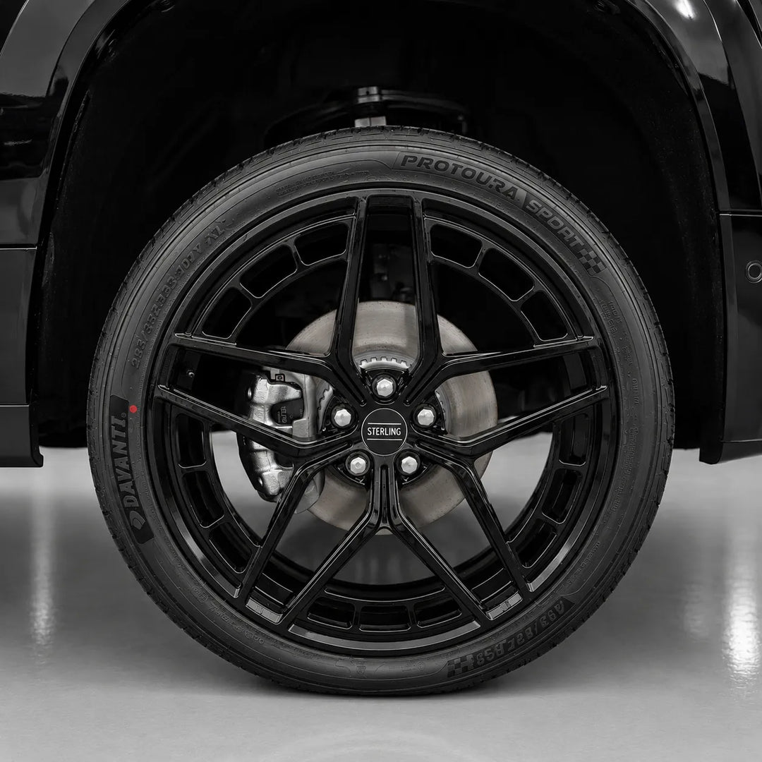 A close-up of a black multi-spoke alloy wheel with a black tire, mounted on a black vehicle. the wheel center cap displays 'STERLING'.