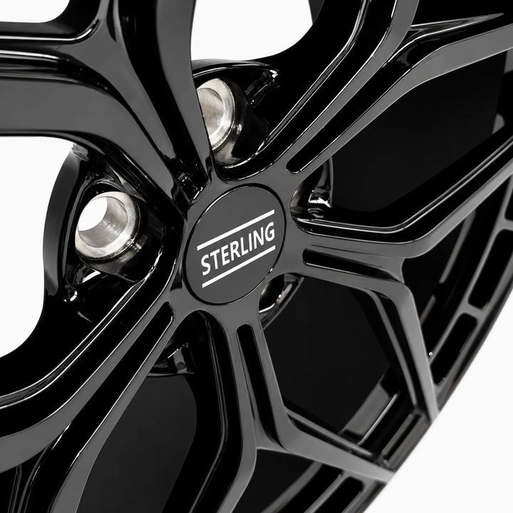 Close-up of a glossy black multi-spoke alloy wheel rim with a circular Sterling center cap and visible silver lug nuts against a white background.