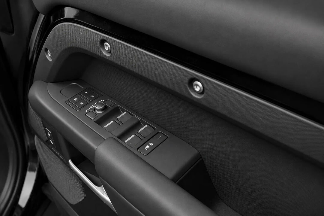 Close-up of a black car Front Driver door panel with window and mirror control buttons, door handle, and textured trim.
