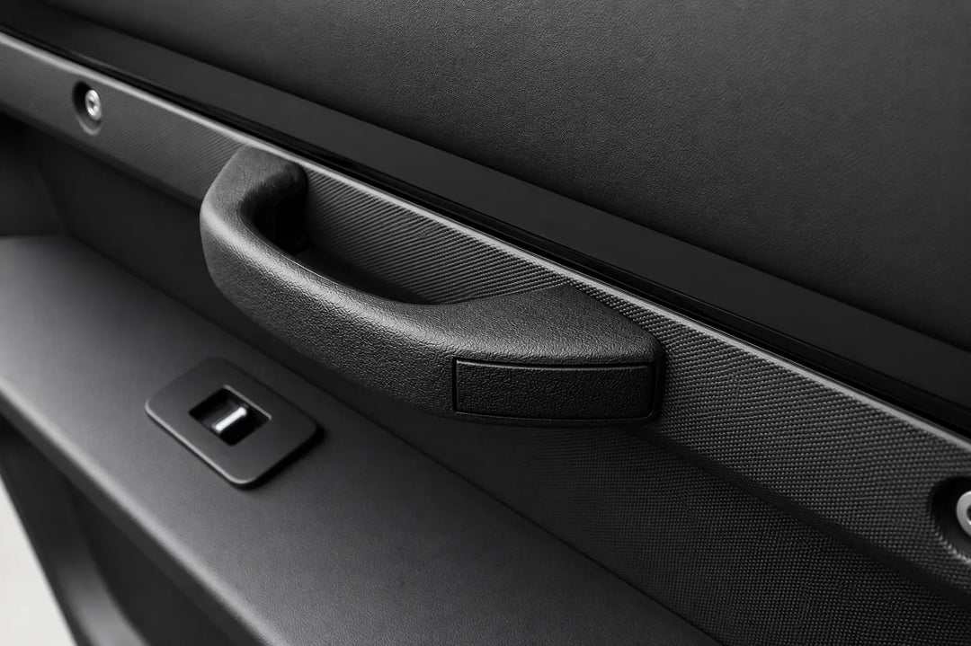 Close-up of a black textured car door handle with an integrated window control switch on a dark gray door panel.
