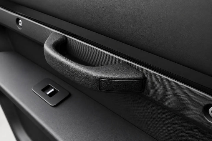 Close-up of a black textured car door handle with an integrated window control switch on a dark gray door panel.