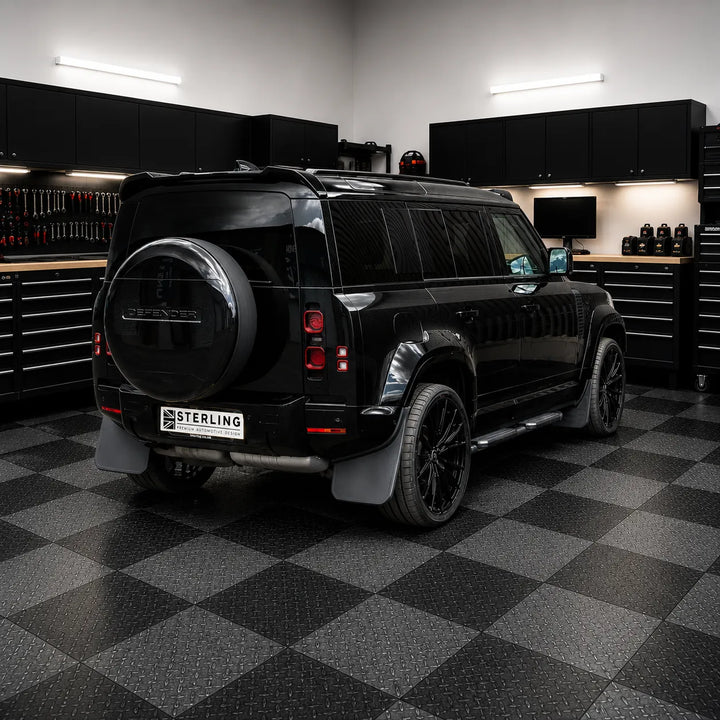 A black Defender SUV with custom black wheels and a license plate reading 'STERLING' is parked inside a modern garage with a black and gray checkered floor.