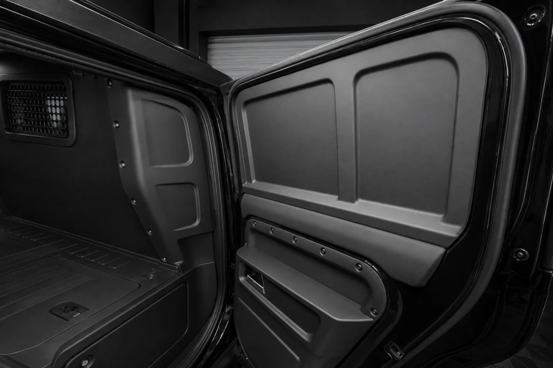 The rear cargo door of a vehicle is open, showing the dark gray molded interior paneling and storage compartment.