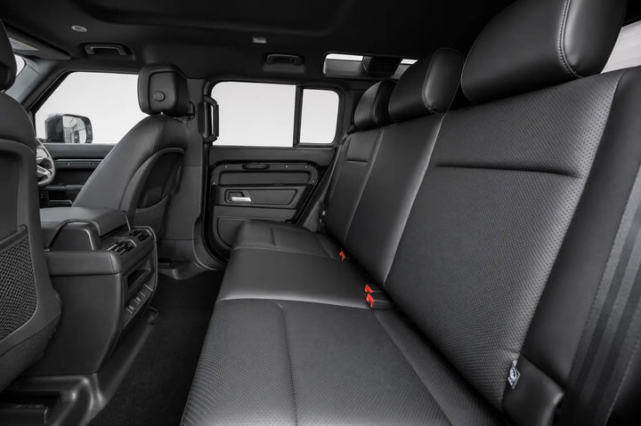 Rear passenger compartment of a black vehicle, showing the back seat with textured black upholstery, headrests, and the interior door panel and center console.