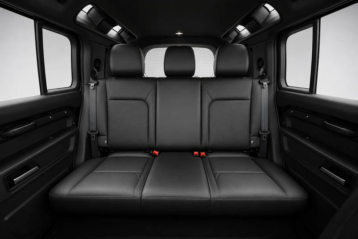 Rear passenger compartment of a vehicle with a black leather three-seat bench, headrests, side windows, and interior door panels.