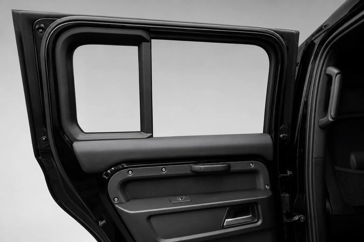 Close-up of a black vehicle door panel with the door open, showing the interior door handle area, window frame, and trim against a light gray studio background.