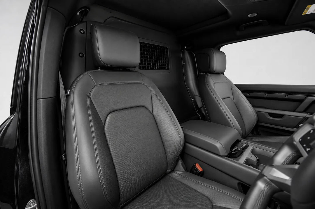 photographed from the open driver-side door with a light gray studio background visible through the window Before the conversion takes place, Black leather front passenger seat and center console of a vehicle interior. Land rover defender 90 l663