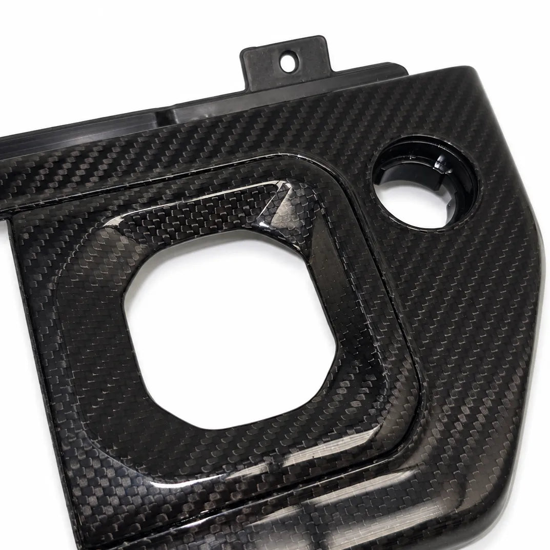 A glossy black carbon fiber panel with a woven carbon texture, featuring a large square cutout and a circular opening, photographed on a white background.