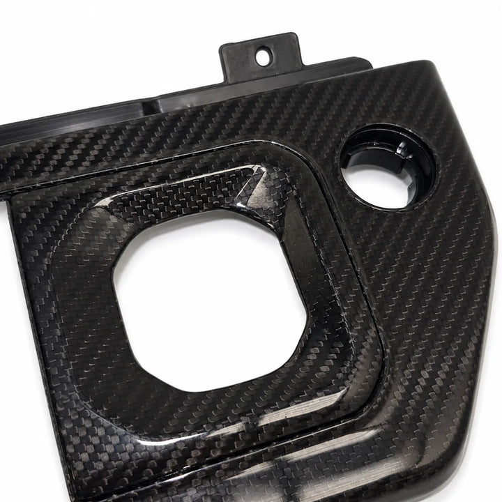 A glossy black carbon fiber panel with a woven carbon texture, featuring a large square cutout and a circular opening, photographed on a white background.