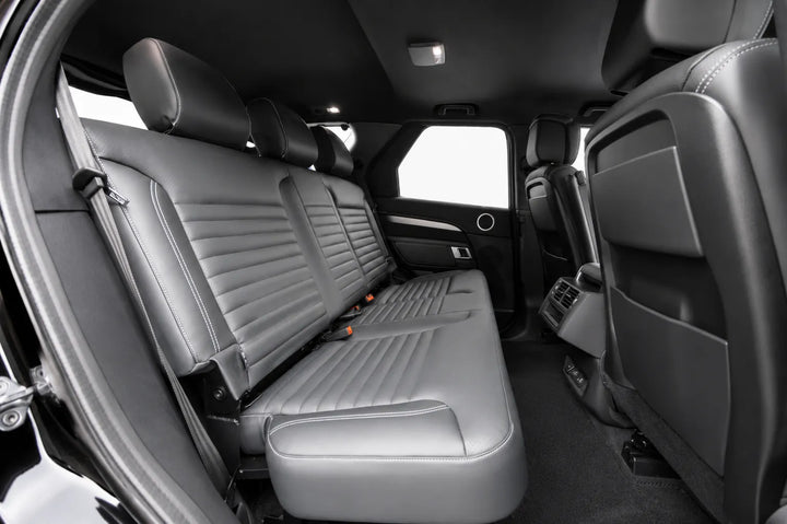 Rear passenger compartment of a vehicle with gray leather seats, showing the second-row bench, front seat backs, door panel, and dark interior.