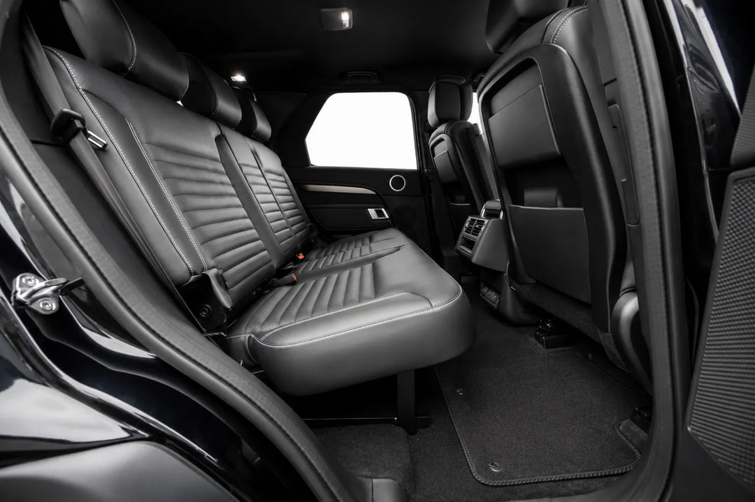 Rear passenger compartment of a black Discovery 5 Disco, showing the back seat with integrated seat belts, the second-row seats, carpeted floor, and open door frame with isofix.