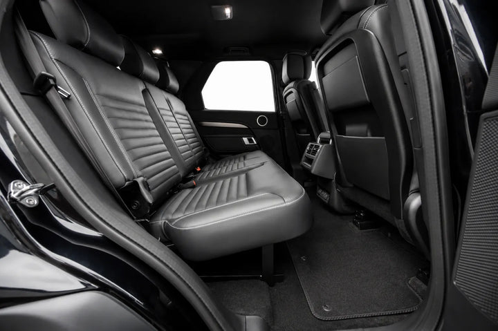 Rear passenger compartment of a black Discovery 5 Disco, showing the back seat with integrated seat belts, the second-row seats, carpeted floor, and open door frame with isofix.