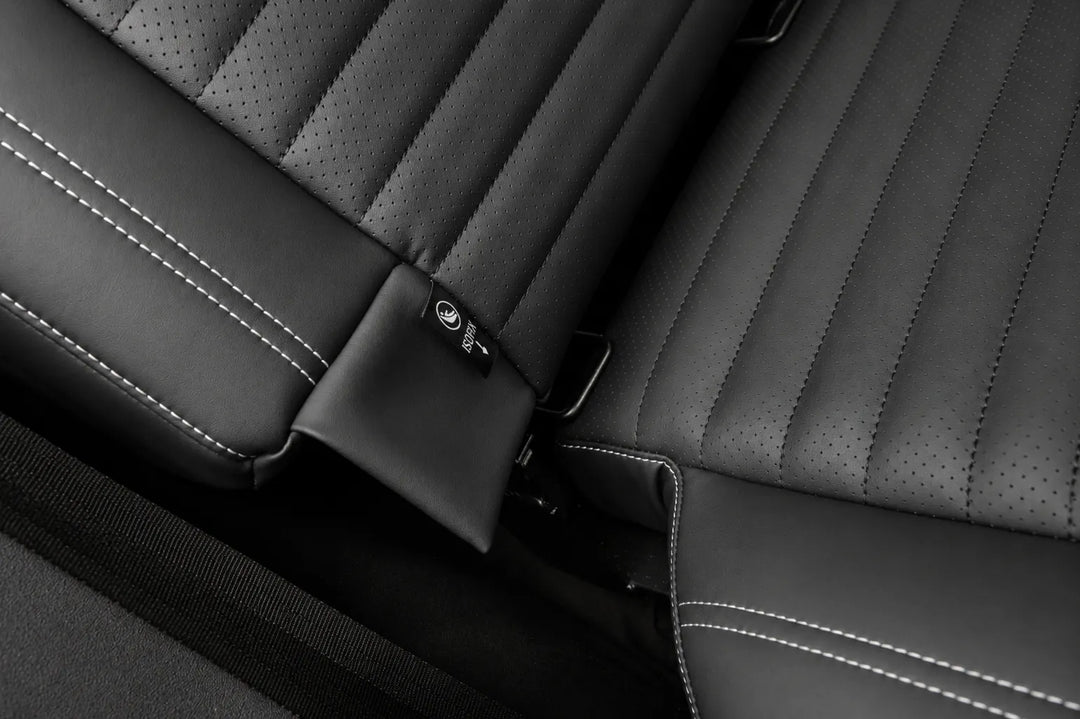 Close-up of a black leather car seat with perforated stitching, contrast white stitching, showing isofix and a matching black headrest.