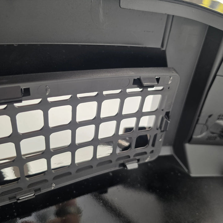A close-up of a dark gray plastic bumper grille panel cover with a grid-like cutout pattern, installed inside the splitter.