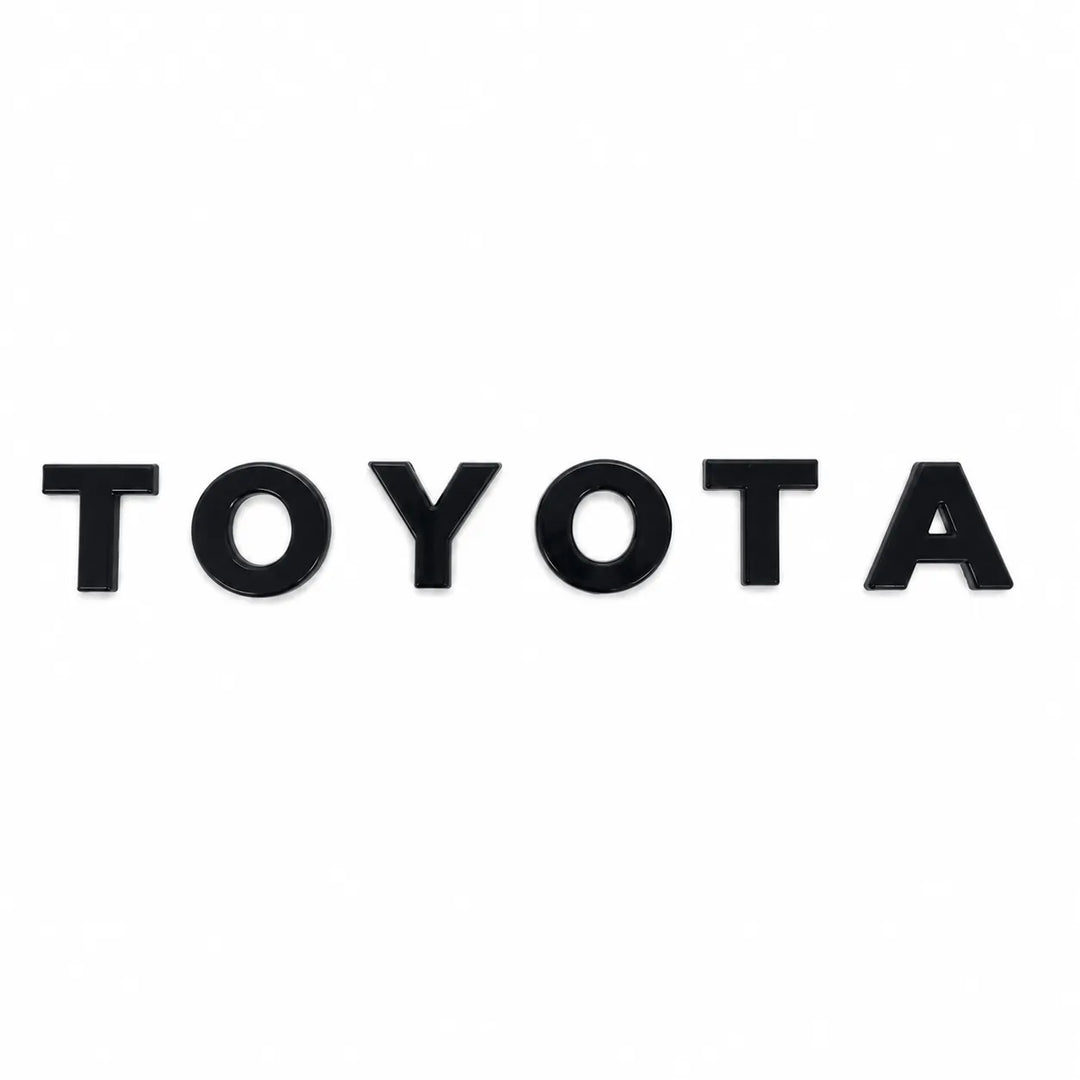 Black glossy grille lettering spelling 'TOYOTA' arranged on a plain white background.