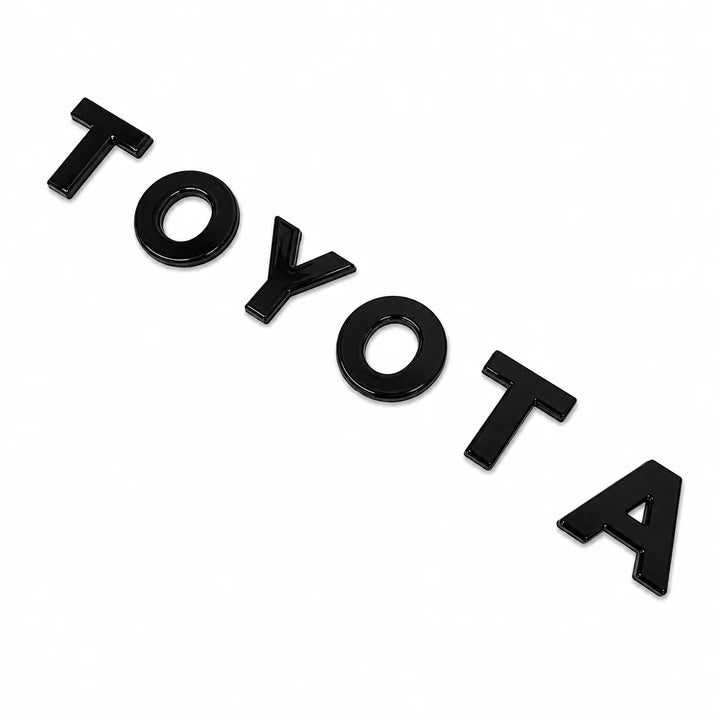 Black glossy 3D Plastic Toyota lettering arranged diagonally on a plain white background.