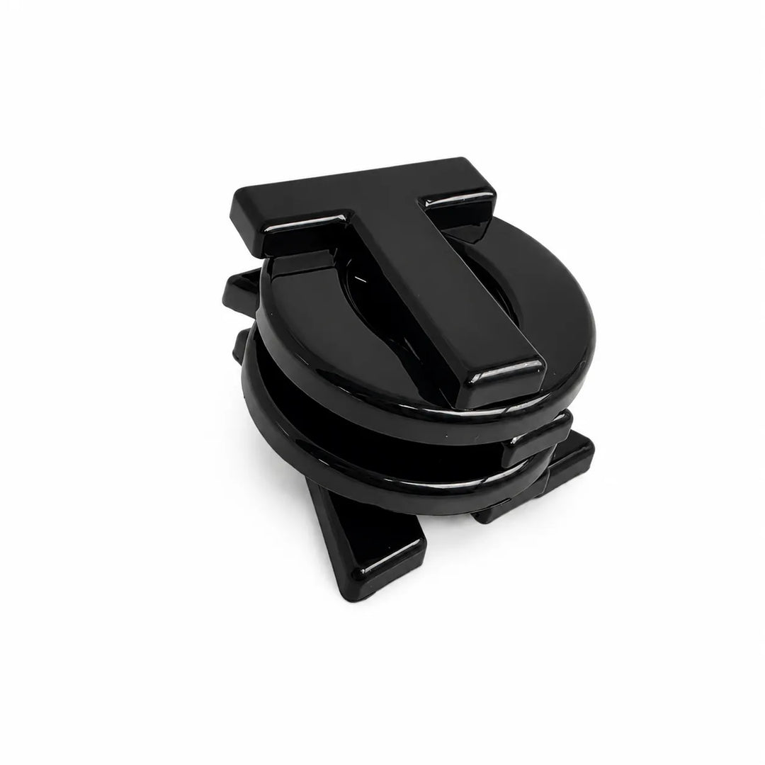 A glossy black metal car accessory with a circular base and a raised letter 'T' on top, photographed on a clean white background.