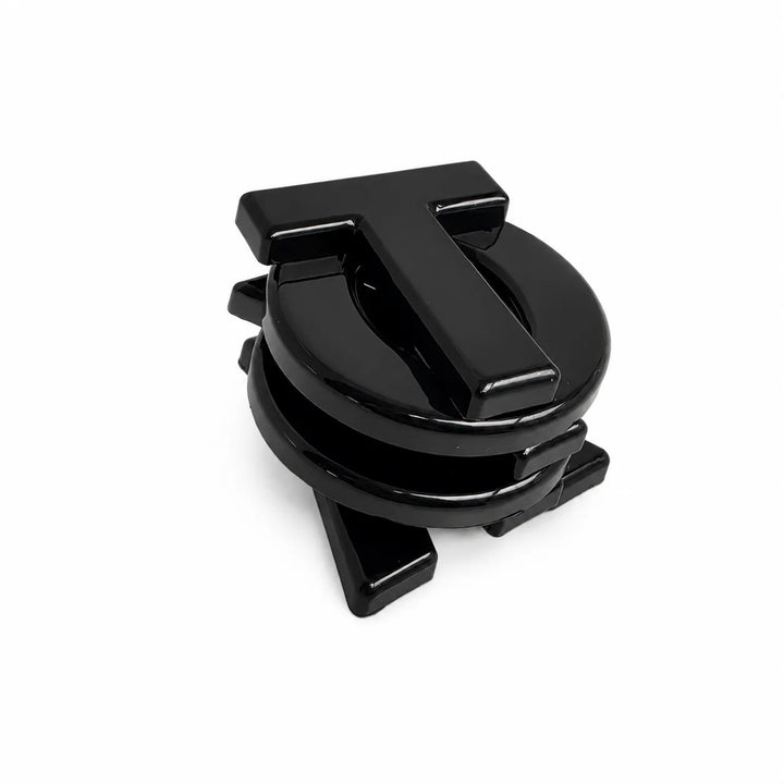 A glossy black metal car accessory with a circular base and a raised letter 'T' on top, photographed on a clean white background.